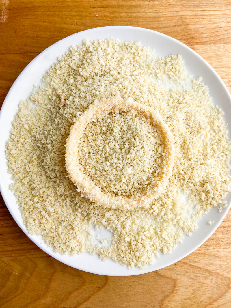 Panko bread crumbs on a white plate with an onion ring in the center. 