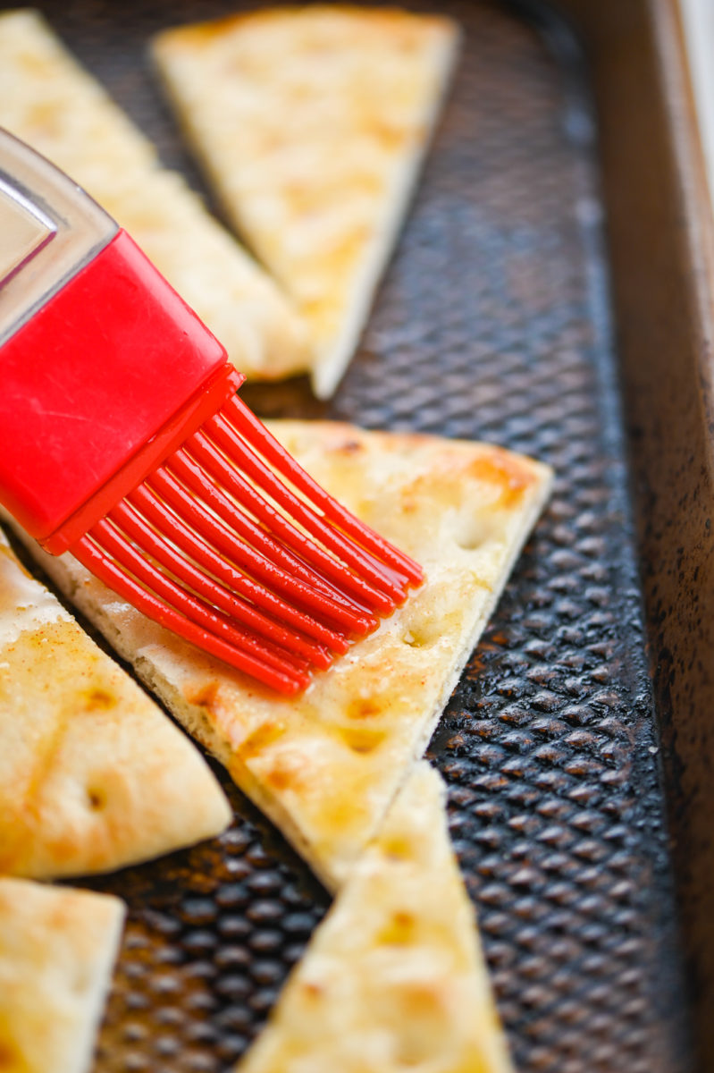 Red pastry brush brushing oil on pita chips. 