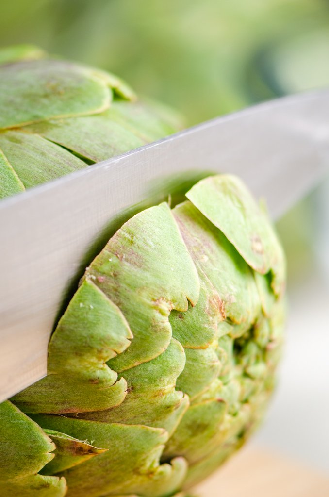 Cutting the top of a raw artichoke with a knife. 