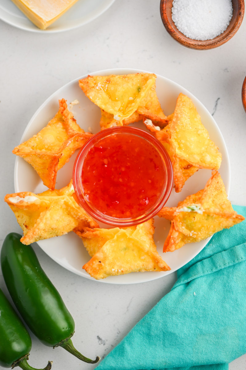 Jalapeño popper wontons on a white plate with Sweet Thai Chili Sauce in a clear ramikin. 