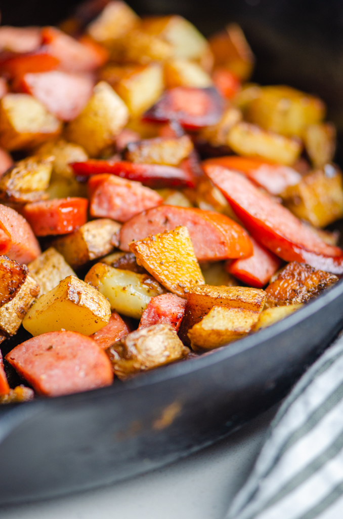 Side angel photo of fried potatoes and kielbasa in a cast iron skillet.