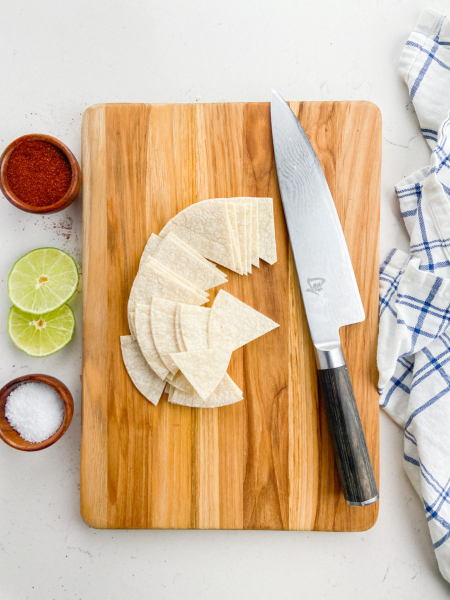Corn tortillas cut into triangles on a cutting board. 