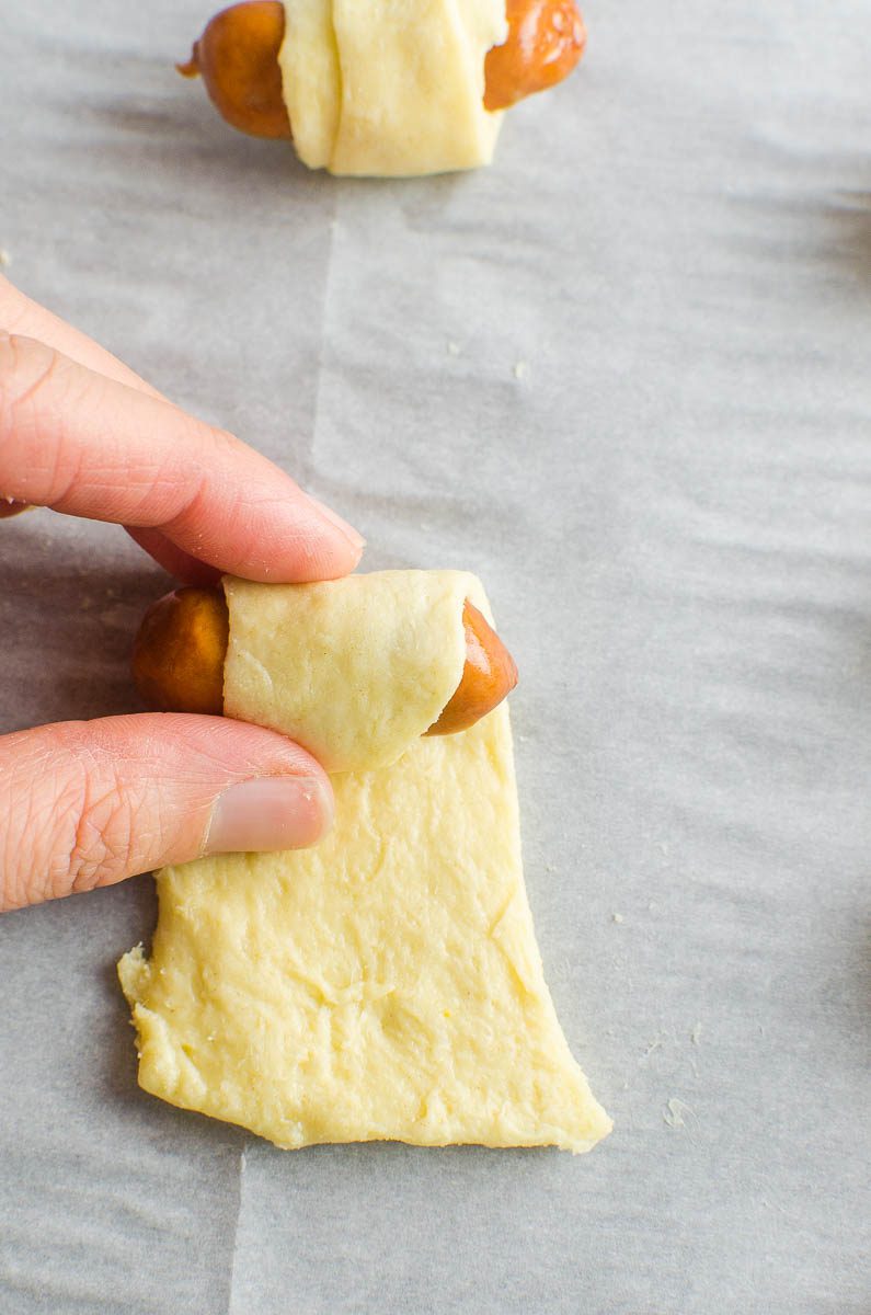 Rolling a cocktail sausage in a crescent roll. 