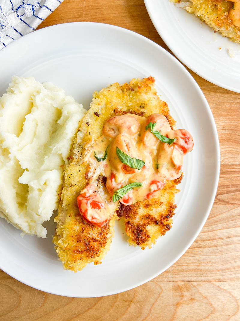 Parmesan Crusted Tilapia with tomato basil sauce on white plate with mashed potatoes
