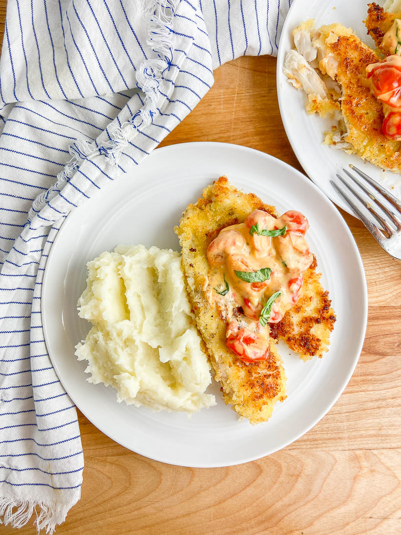Overhead photo of parmesan crusted tilapia on a white plate with wooden cutting board. 