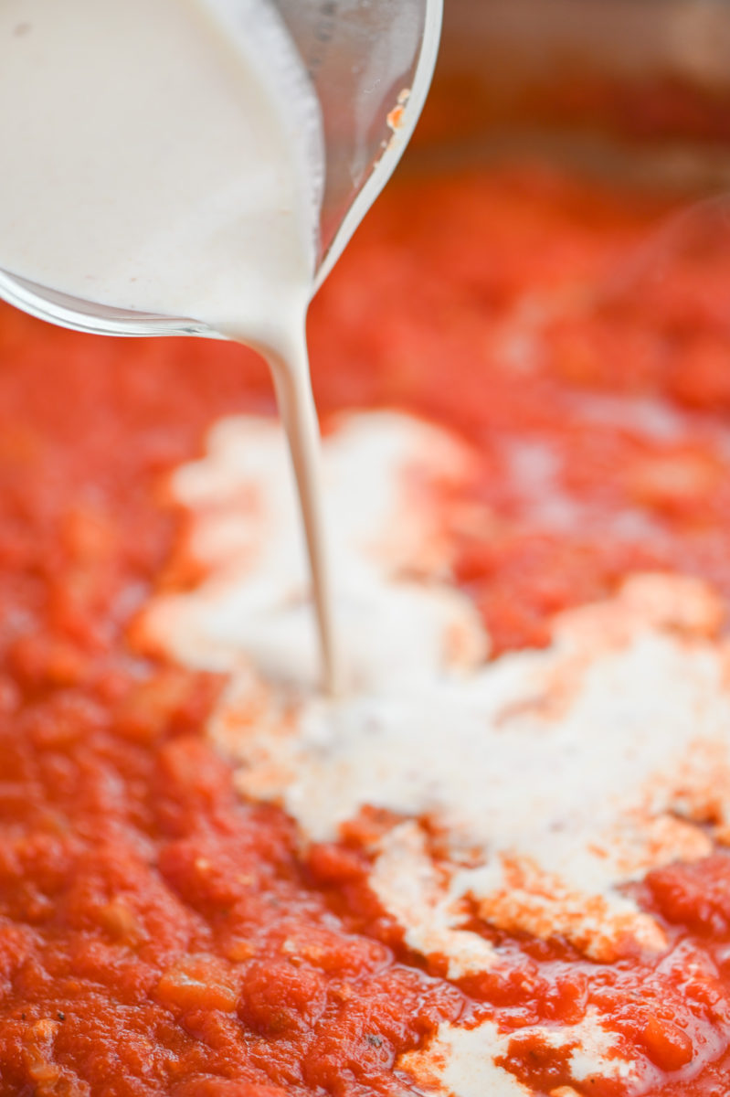 Pouring cream into tomato sauce.