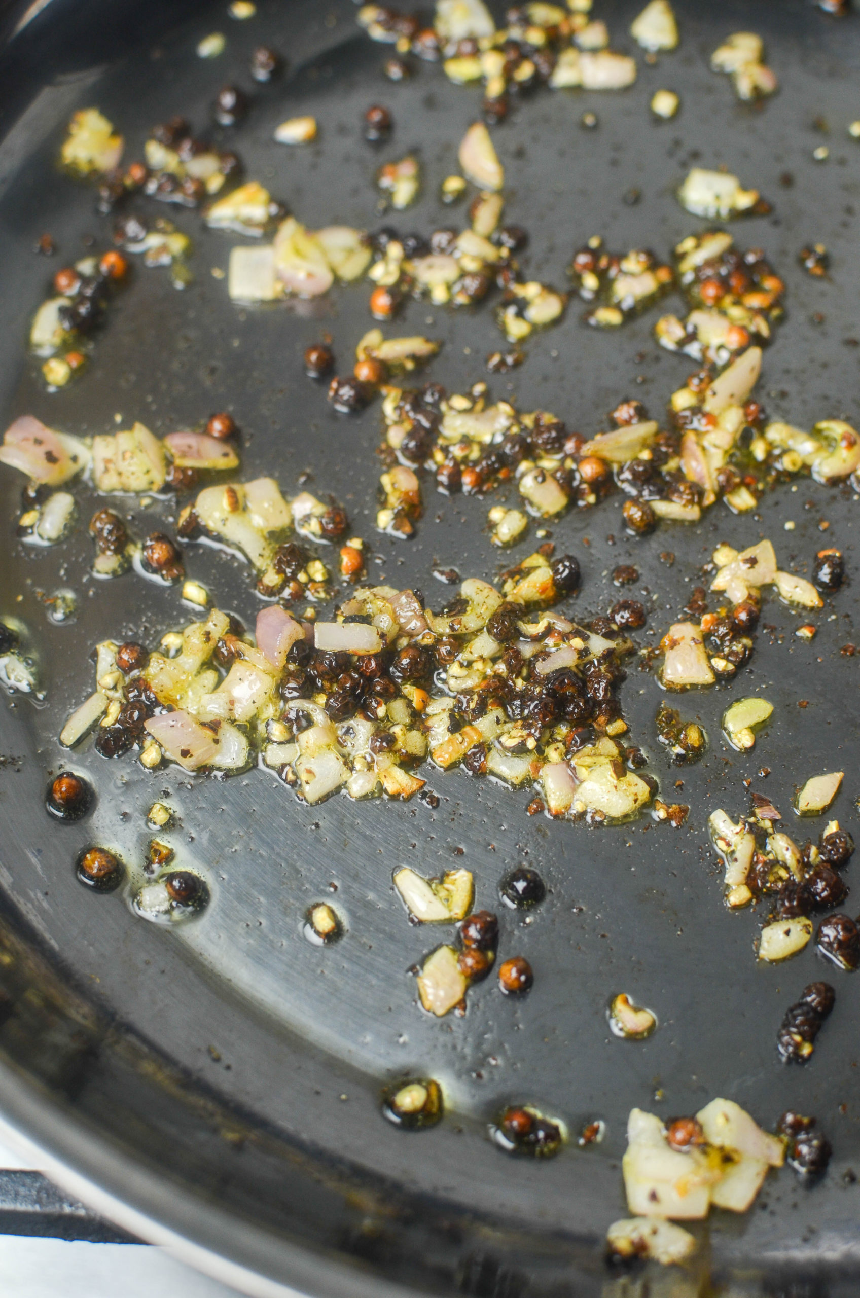 Shallots and peppercorns in a skillet. 