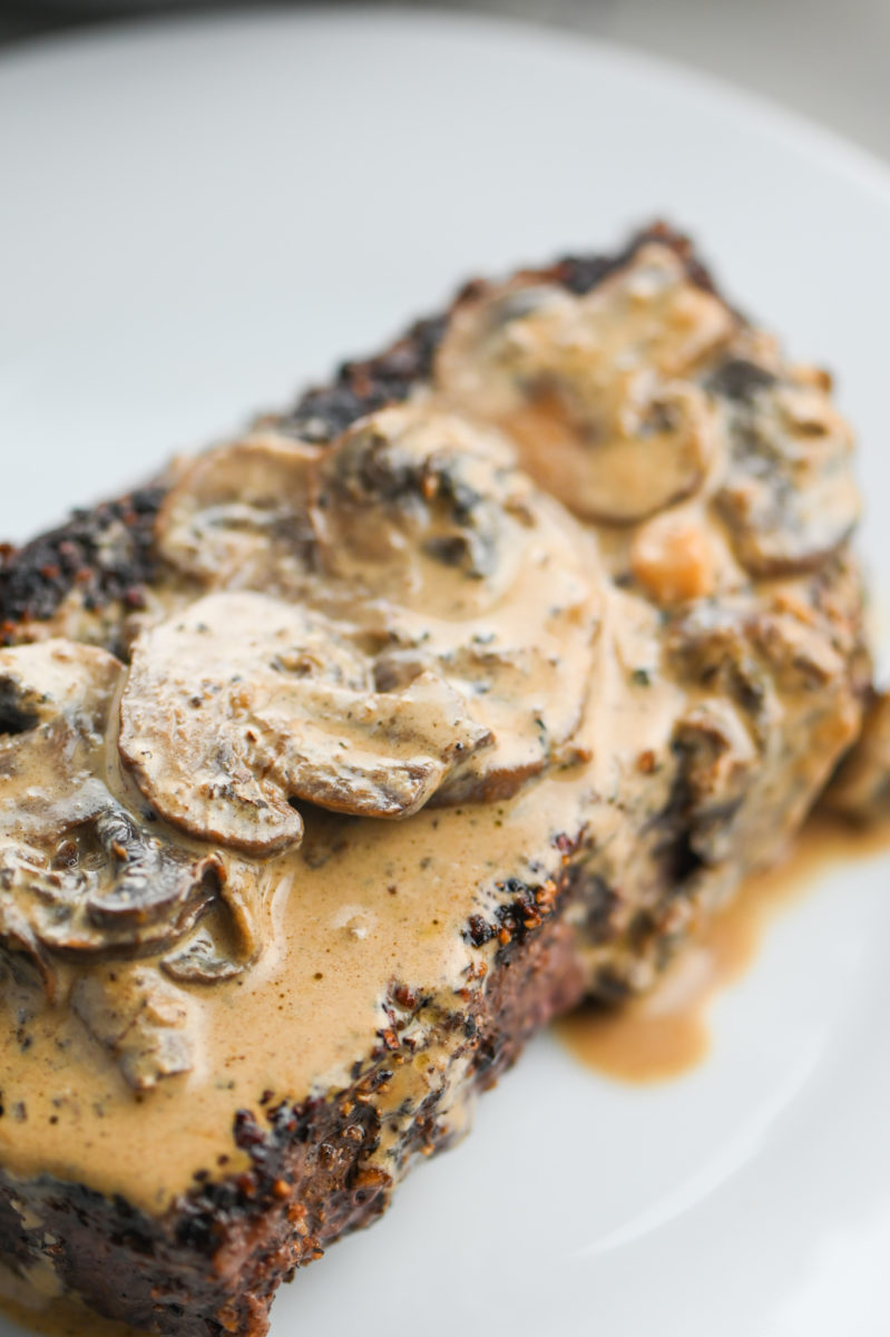 Top sirloin steak with mushroom cream sauce on top on white plate. 