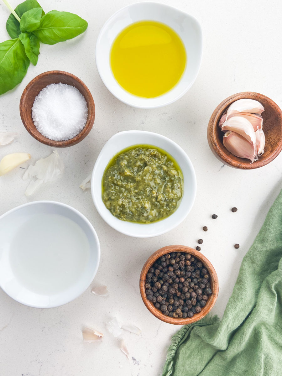 Overhead photo of pesto vinaigrette ingredients on white background. 