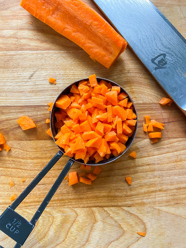 Diced carrots in a measuring cup on a wooden cutting board. 