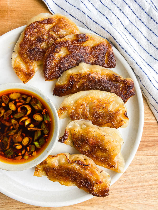 Potstickers on a white plate with sauce. 
