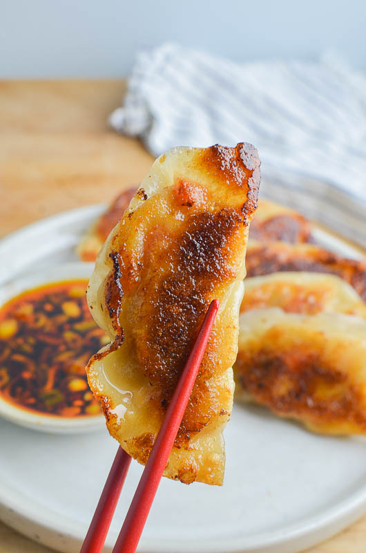 Holding a pork potsticker with two red chopsticks. 