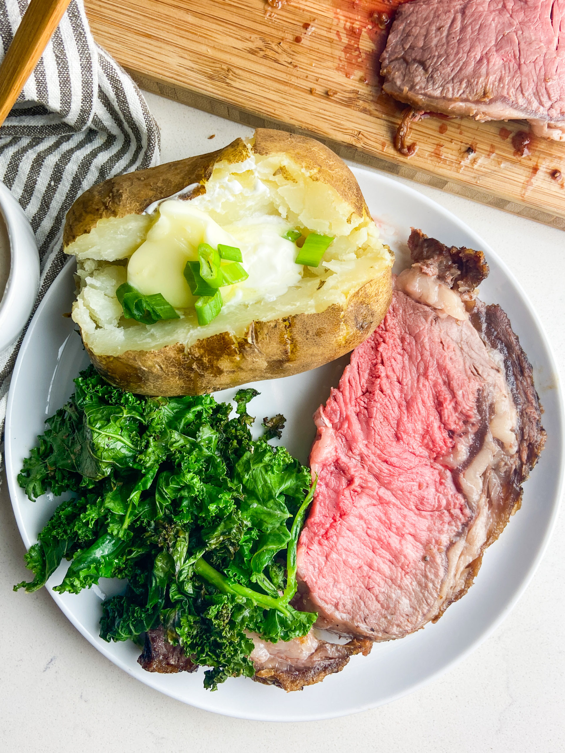 Prime rib on plate with baked potato and sauteed kale. 