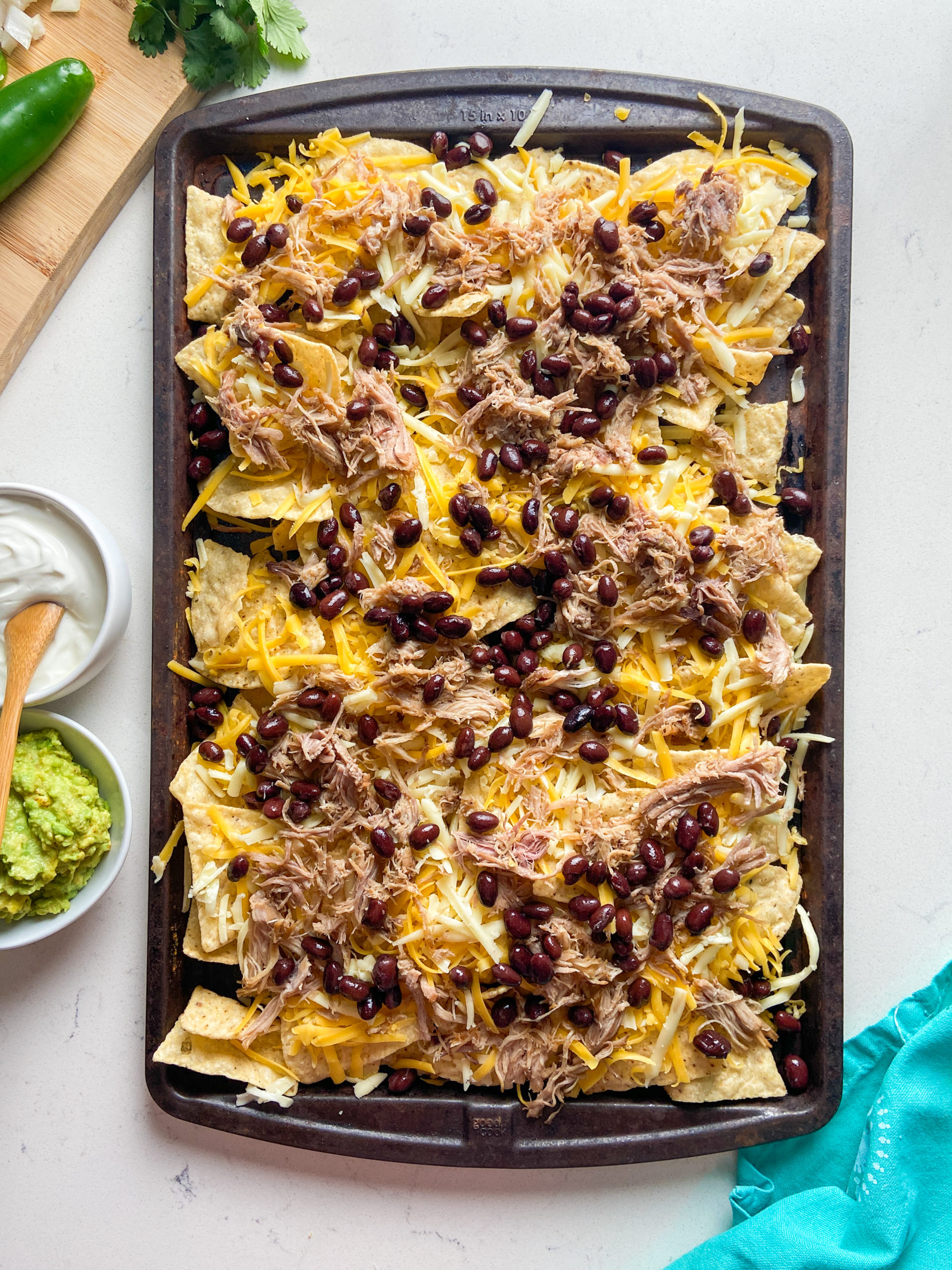 Tortilla chips on a sheet  pan topped with cheese, pulled pork and black beans. 