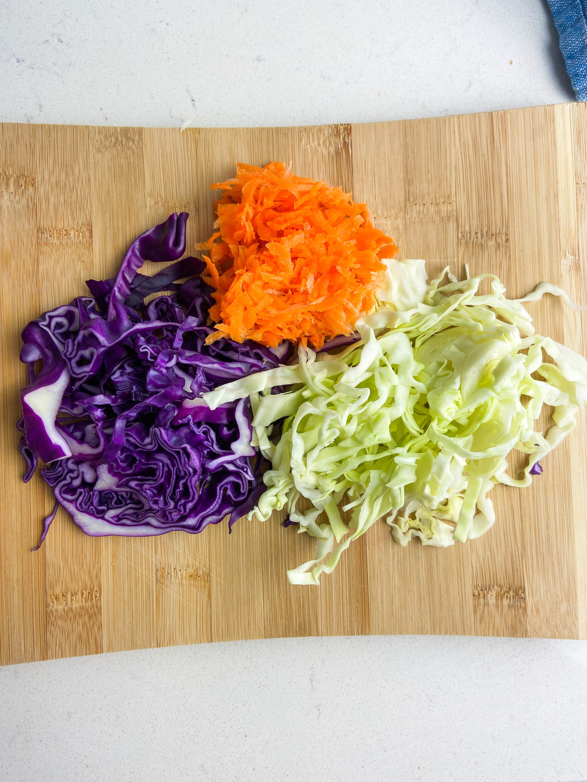 Sliced red and green cabbage and carrots on a wooden cutting board. 