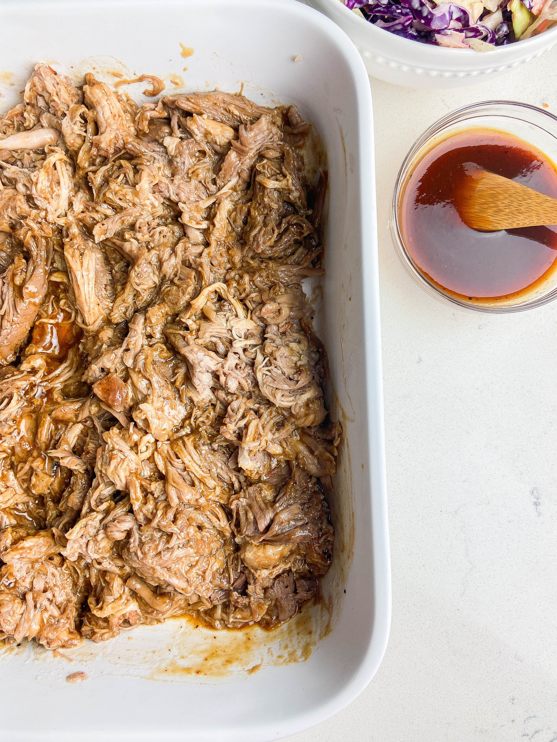 Overhead photo of pulled pork on a white background with a bowl of BBQ sauce. 