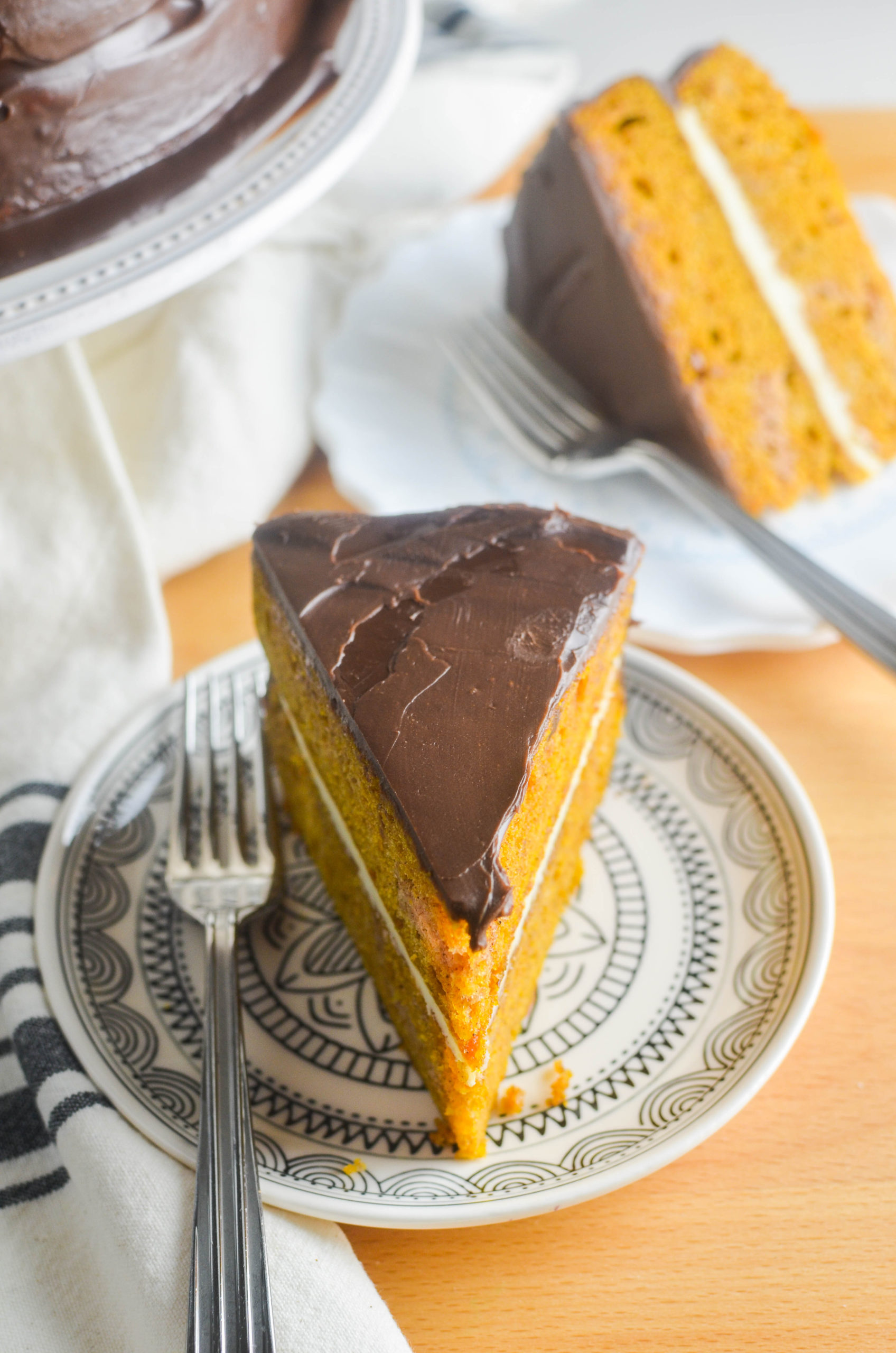 Slice of pumpkin cake with chocolate ganache on a plate. 