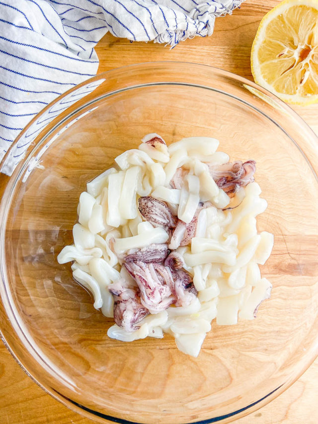 Raw calamari in a glass bowl with lemon. 