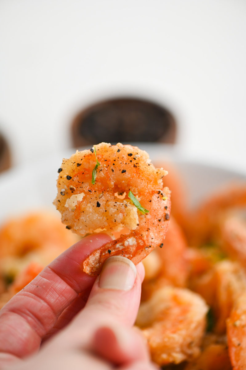A hand holding a salt and pepper shrimp. 