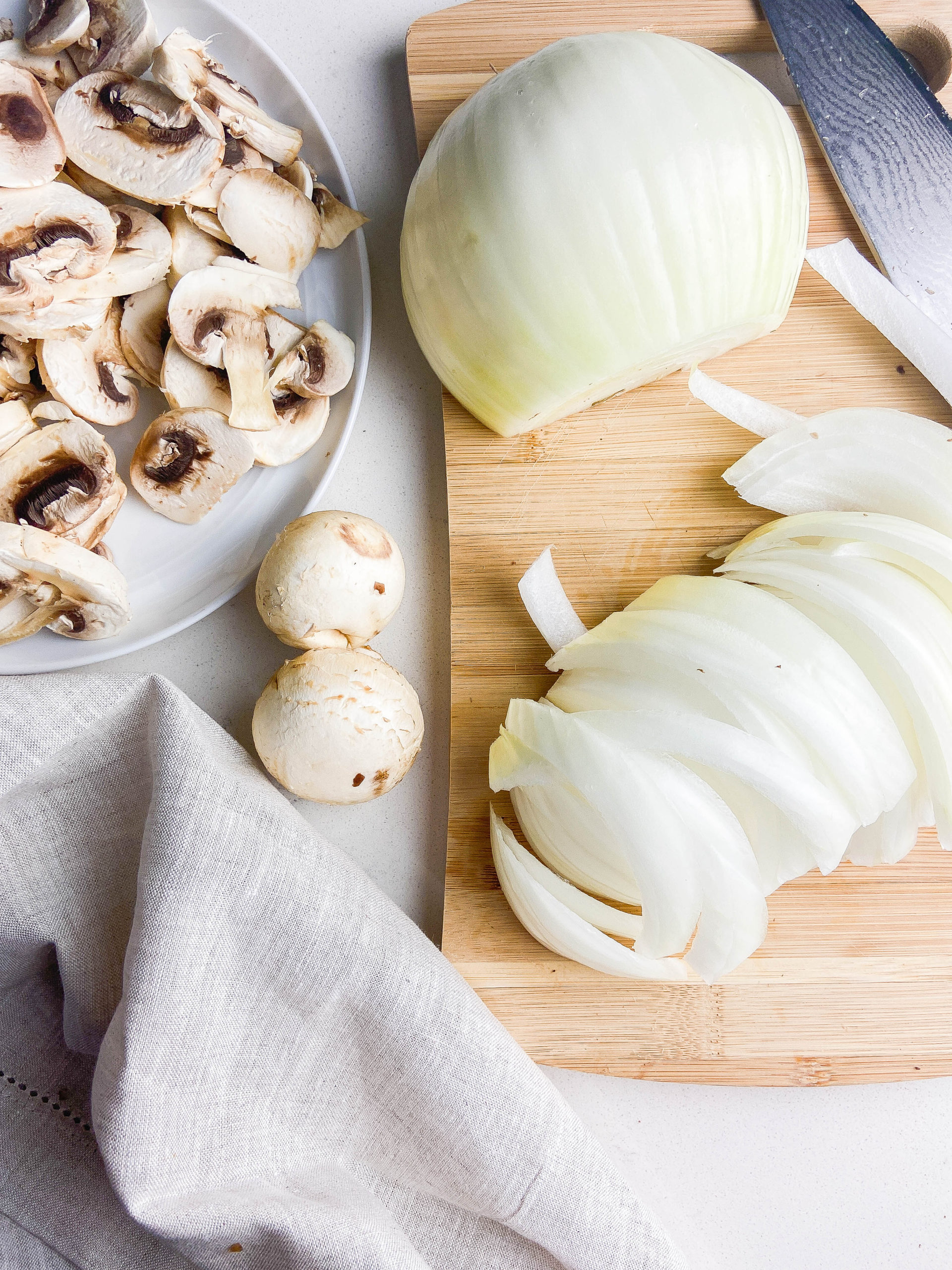 Overhead photo of sliced onions and mushrooms on wooden cutting board. 