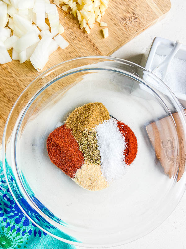 Spices in a glass bowl with a cutting board and blue towel off to the side. 