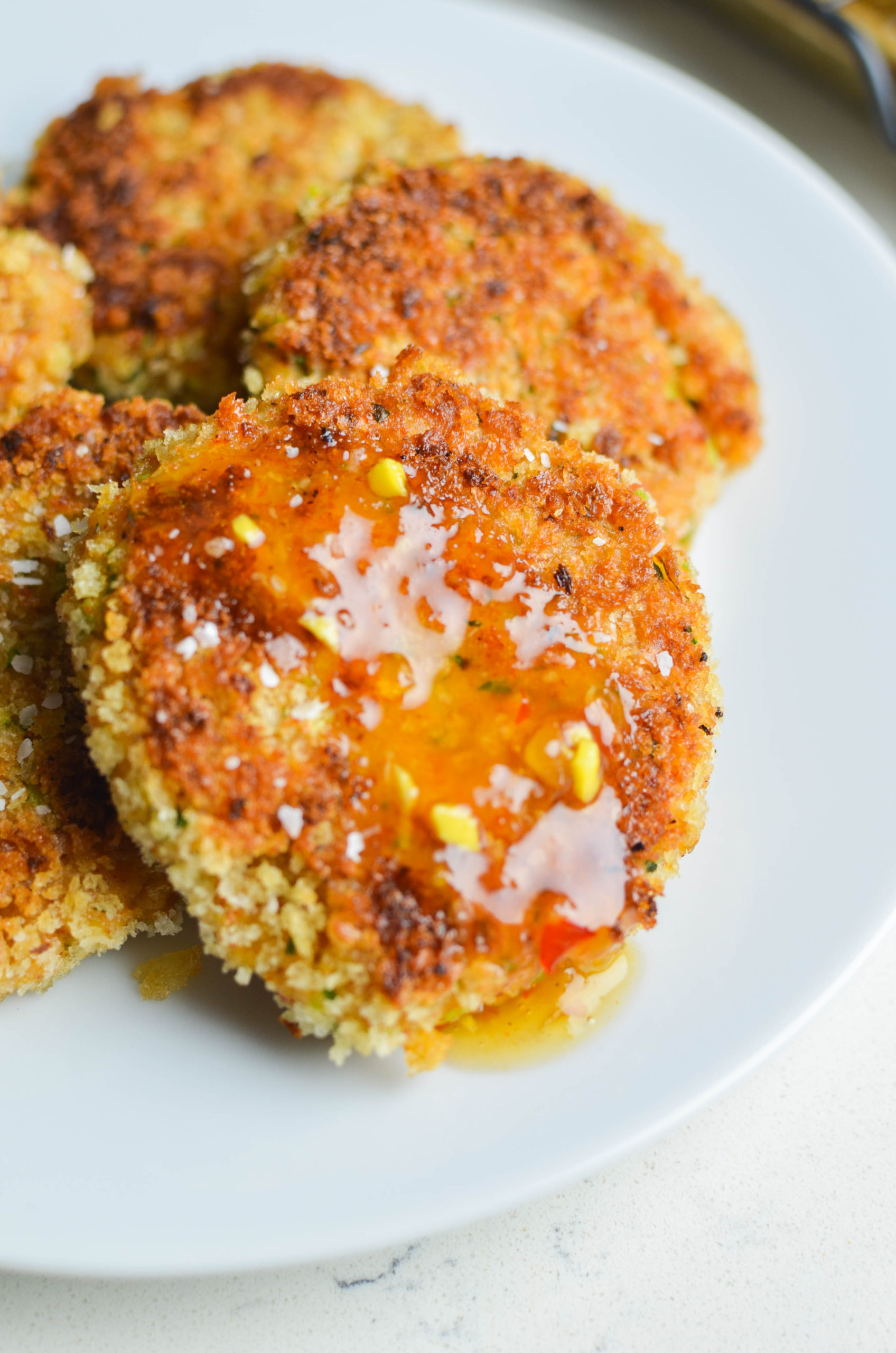 Side angle photo of shrimp cakes with sauce on white plate. 