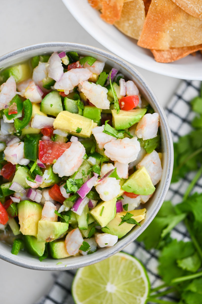 Overhead photo of shrimp ceviche in a bowl with a lime, tortilla chips and cilantro in the background.