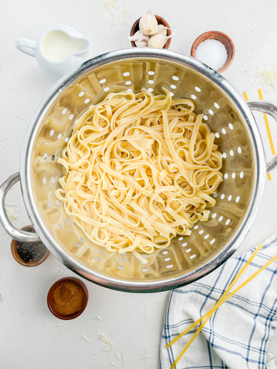 Cooked fettuccine in a silver colander. 