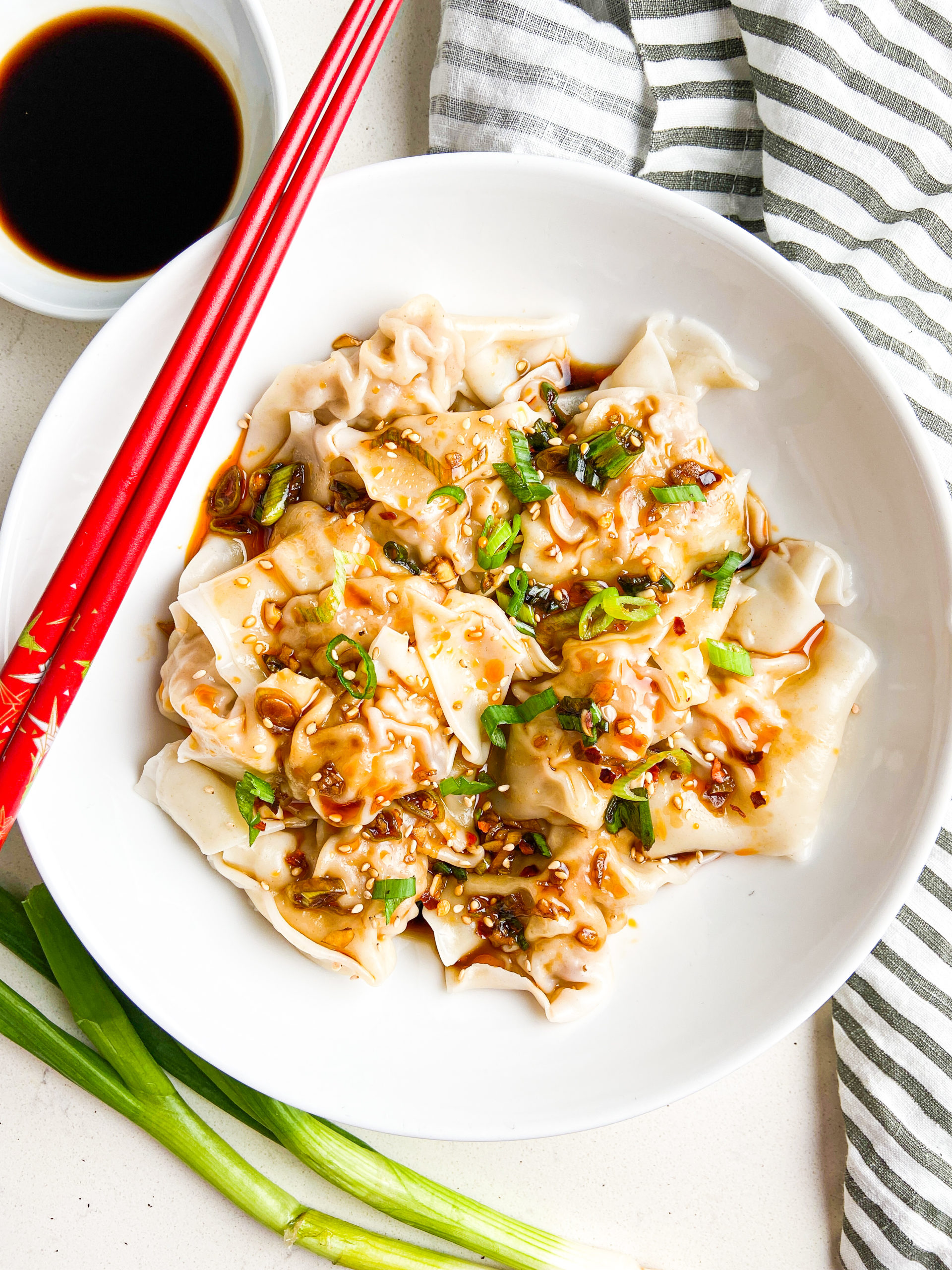 Overhead photo of shrimp and pork wontons in spicy sauce in white bowl with red chopsticks. 