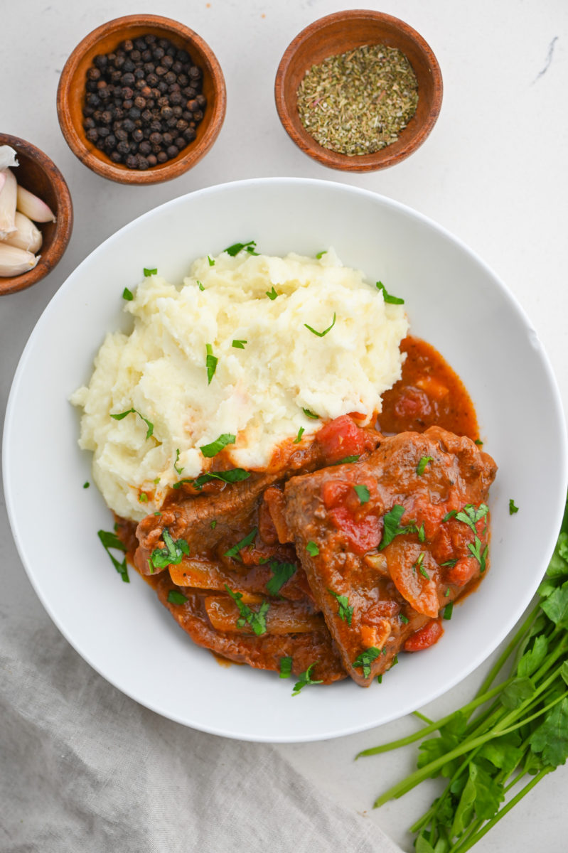 Swiss steak on white plate with mashed potatoes.