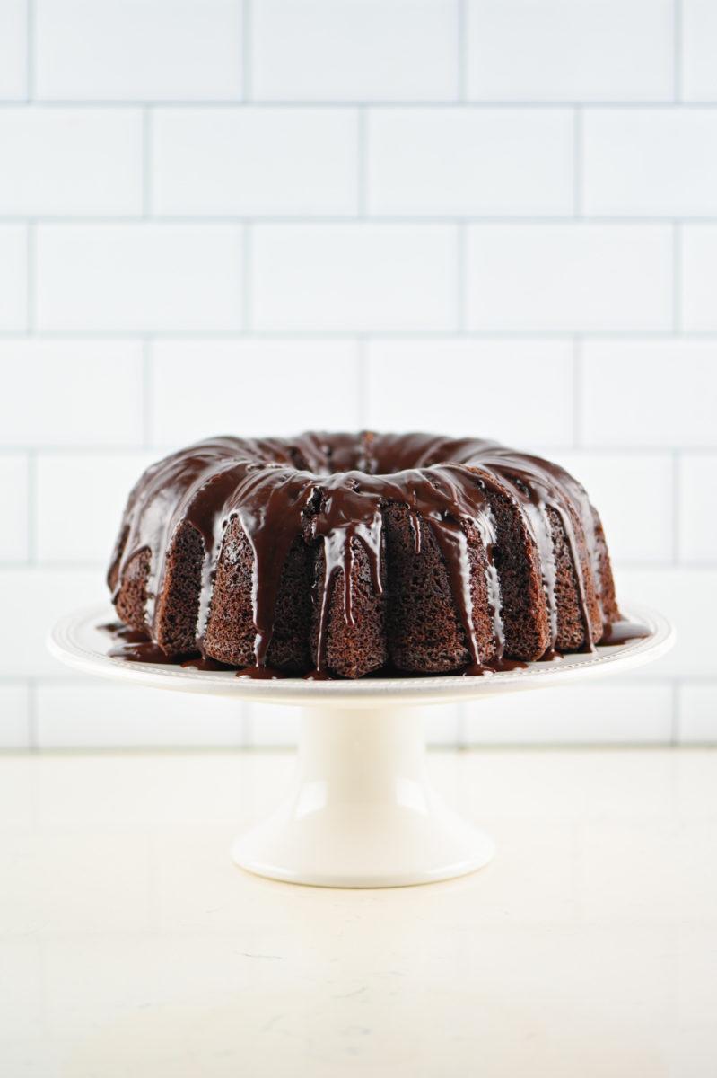 Triple Chocolate Bundt Cake on white cake stand with white background. 