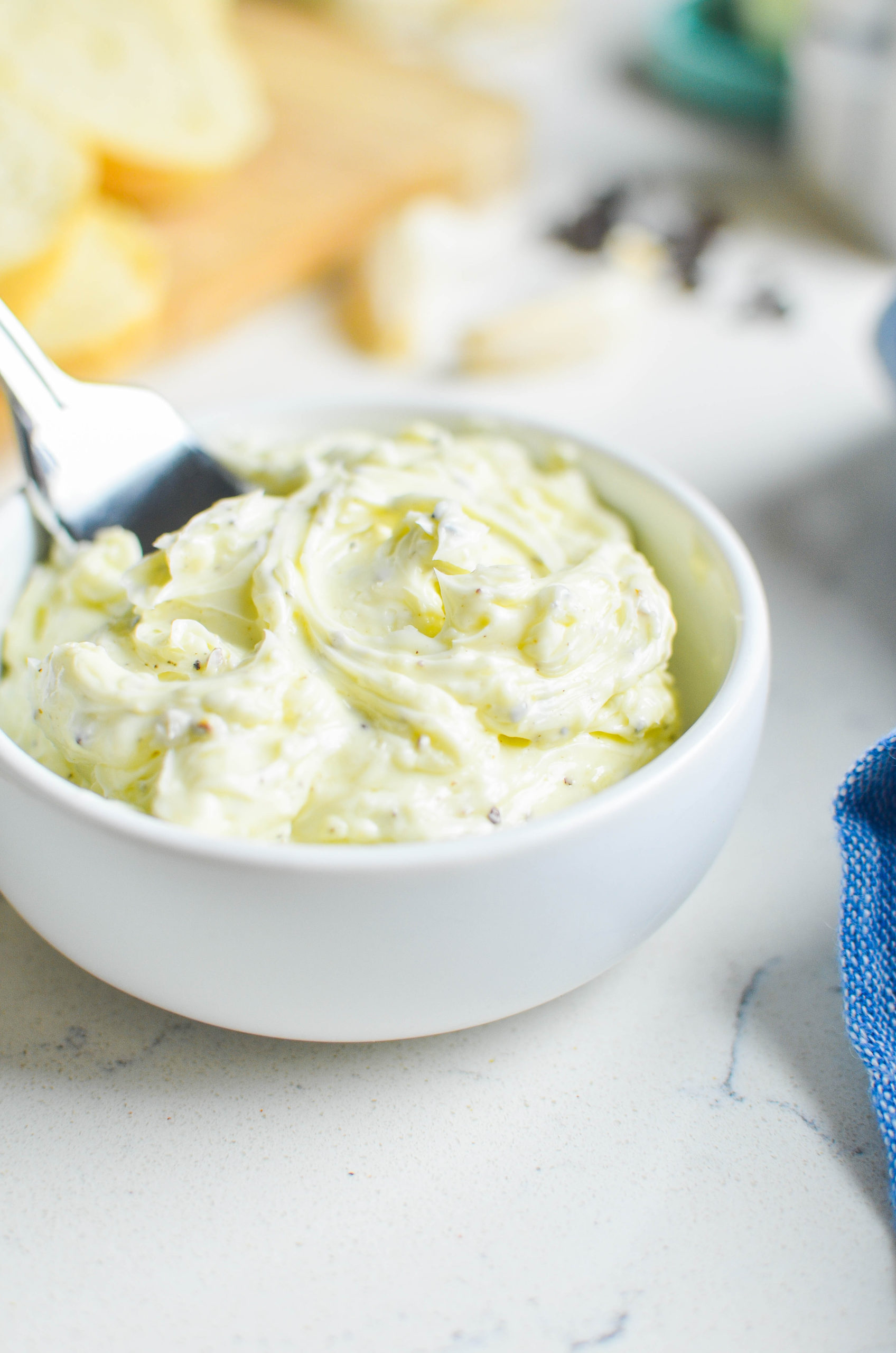 Side view of whipped butter in a white bowl on a white surface. 