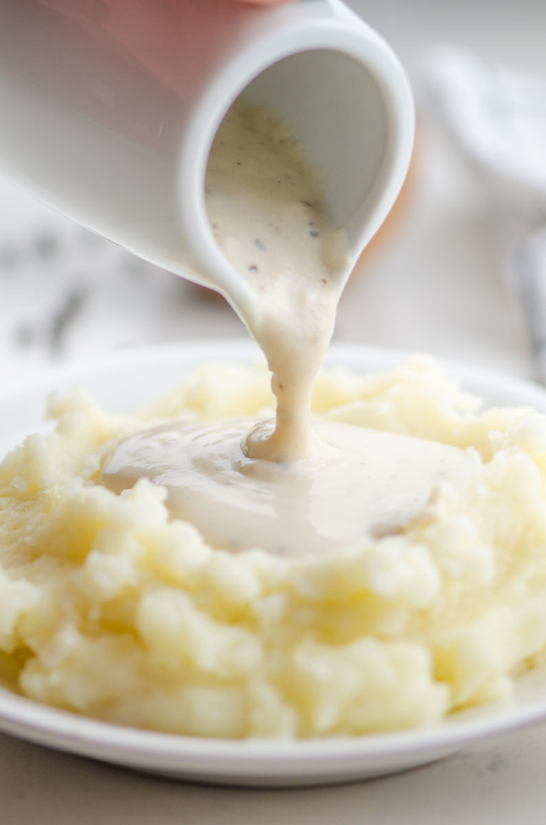 Pouring white country gravy on mashed potatoes.